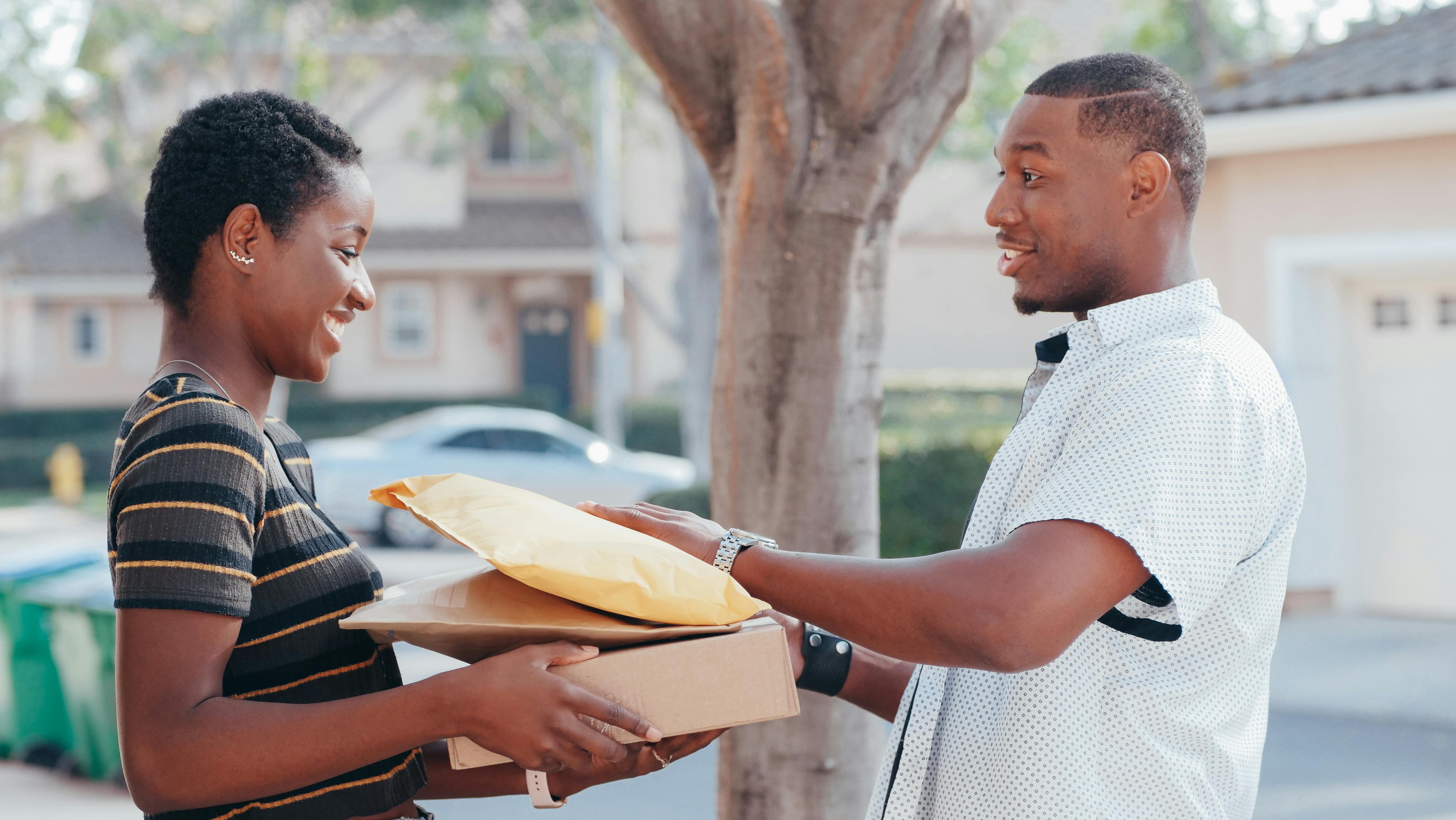 A black man wearing a white shirt delivery packages to a woman