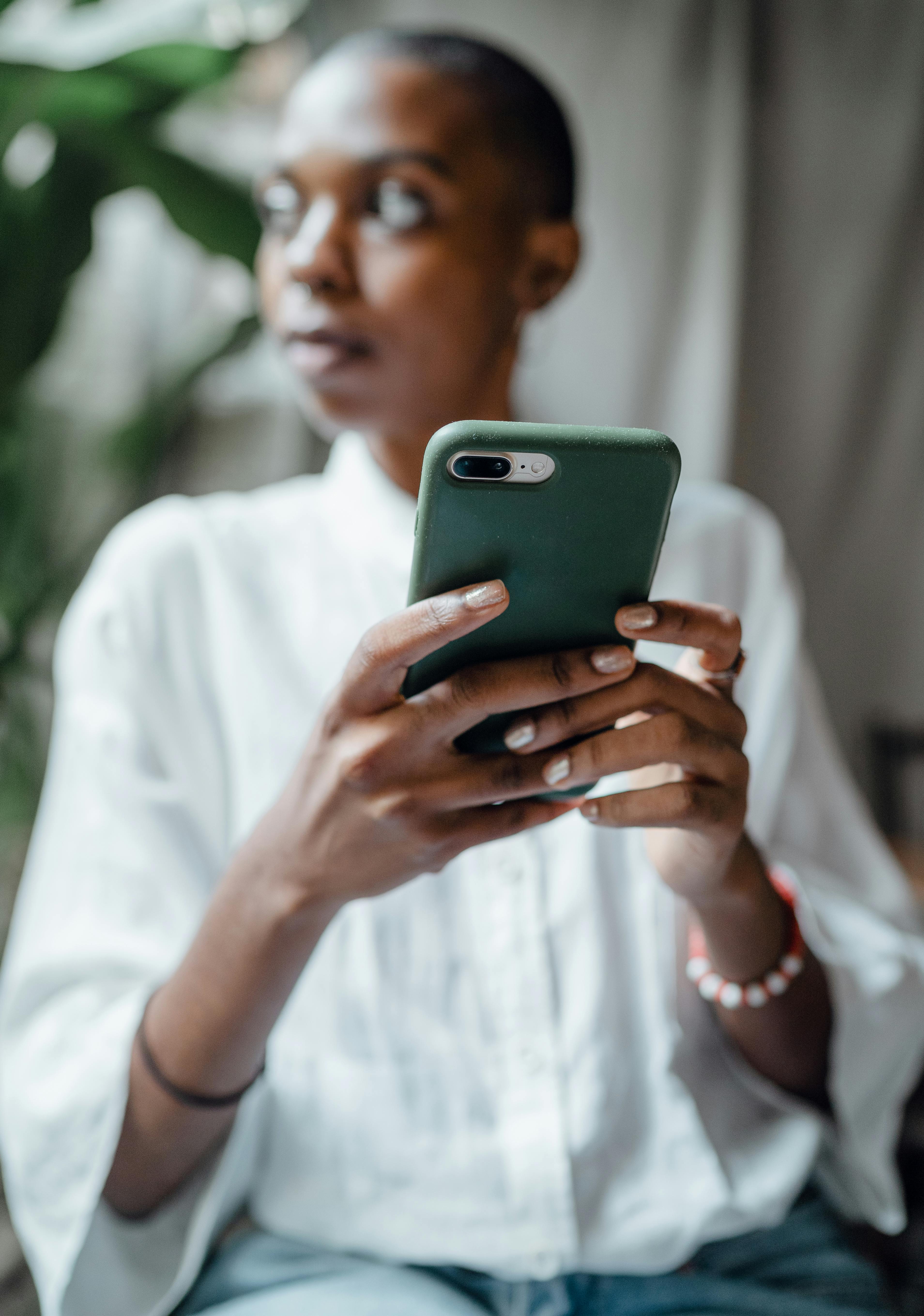 Black woman holding her cell phone and looking out the window in deep thought